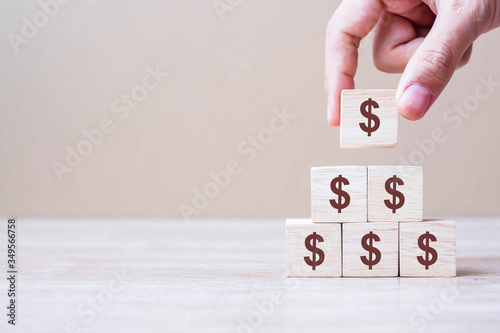 Businessman hand holding wooden blocks with the American Dollar symbol. Money, cash, currency and investment concept.