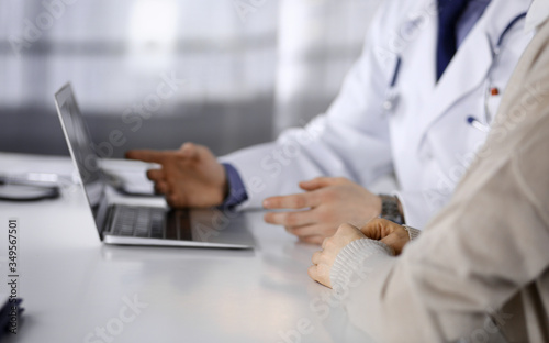 Unknown male doctor and patient woman discussing something while sitting in clinic and using laptop. Best medical service in hospital, medicine, pandemic stop