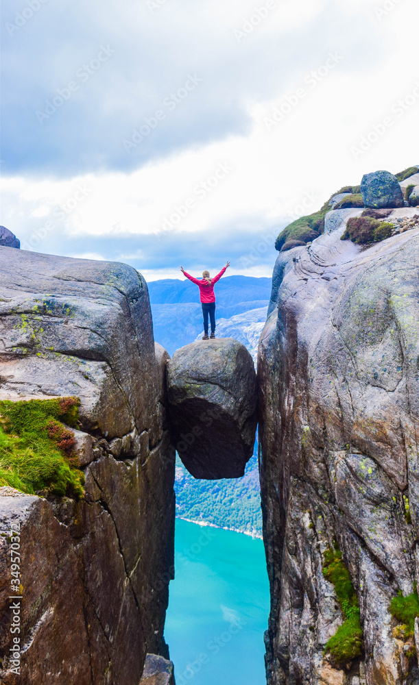 Φωτογραφία The tourist hiker girl standing on top of Kjeragbolten - the most dangerous stone in the world