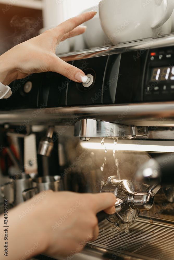 A close photo of a purging a grouphead thoroughly with hot water in the espresso machine in a coffee shop. A female barista works in a cafe.