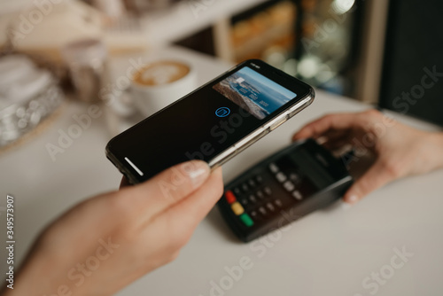 A lady paying for her latte with a smartphone by contactless PAY PASS technology in a cafe. A female barista holds out a terminal for paying to a client in a coffee shop.