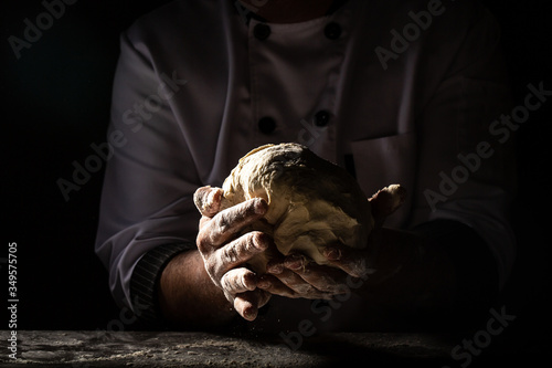 Beautiful and old women's hands knead the dough from which they will then make bread, pasta or pizza. A cloud of flour flies around like dust. Food concept.