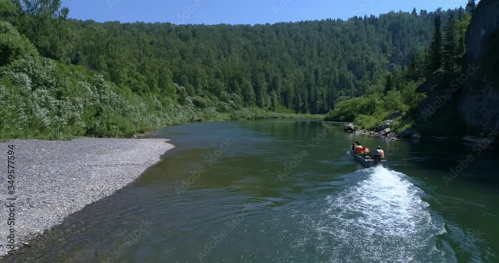 AERIAL VIEW: People in the Long tail boat. Drone view of a boat floating through the blue clear waters of a mountain river in the Siberian taiga. Summer Day AERIAL VIEW: People in the Long tail boat. Drone view of a boat floating through the blue clear waters of a mountain river in the Siberian taiga. Summer Day