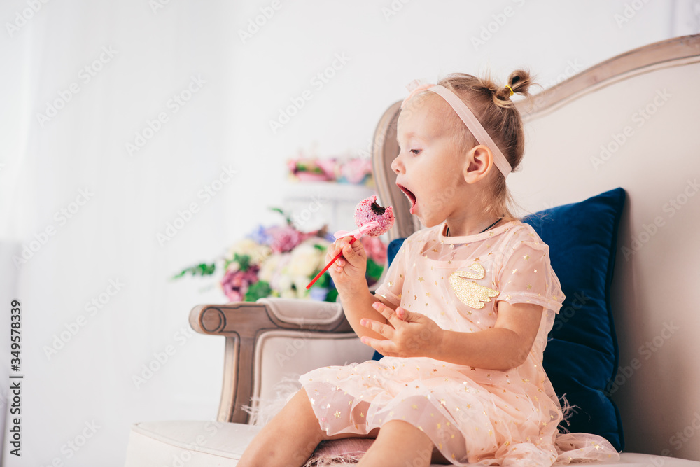 Beautiful girl playing with cupcake. Birthday baby. Model, happy. Little girl with cake. Childhood. Little child girl in a beautiful dress eats a cake while sitting on a sofa in the living room