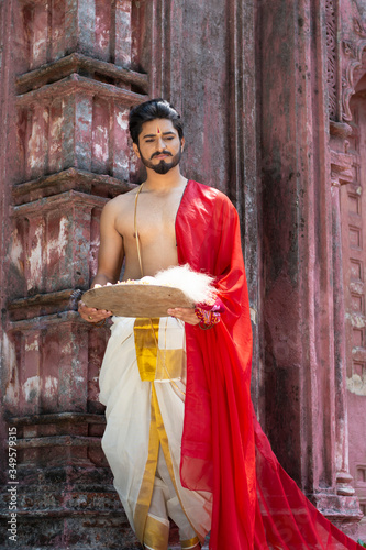 Portrait of an Indian pujari/ worshiper in bare body Indian ethnic traditional wear worshiping in a temple/ mandir. Indian lifestyle and ethnic wear. © abir