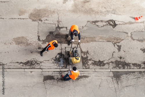 Road workers in orange vests repair the road. Pit removal and patching. View from above. works of replacing asphalt parts