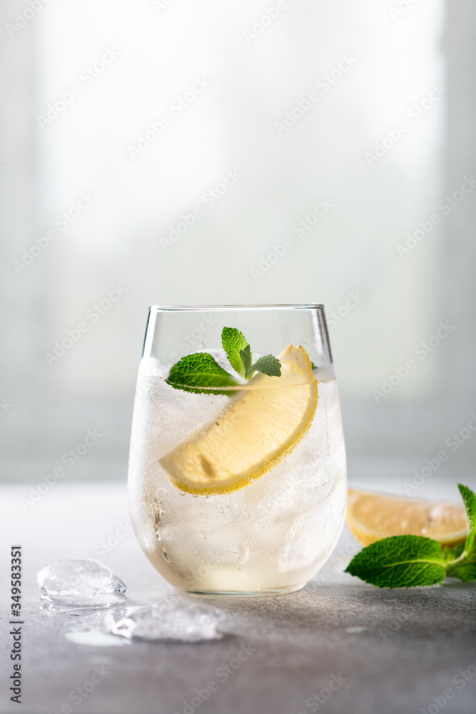 cold lemonade with ice, mint and lemon in a glass on a light background, place for text