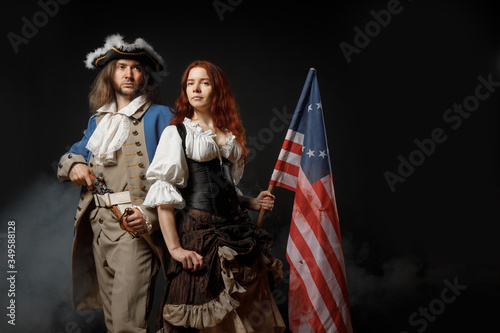 Man in form of officer of United States War of Independence and girl in historical dress of 18th century. July 4 is US Independence Day. Studio photo on black background