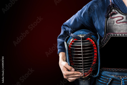 male in in tradition kendo armor with helmet in hand. shot in studio. isolated on dark red background