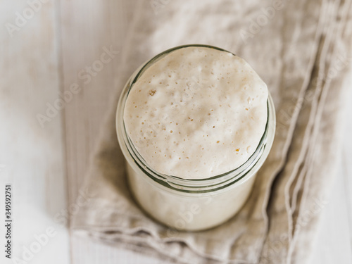 Wheat sourdough starter. Top view of glass jar with sourdough starter on white wooden background. Copy space for text or design. photo