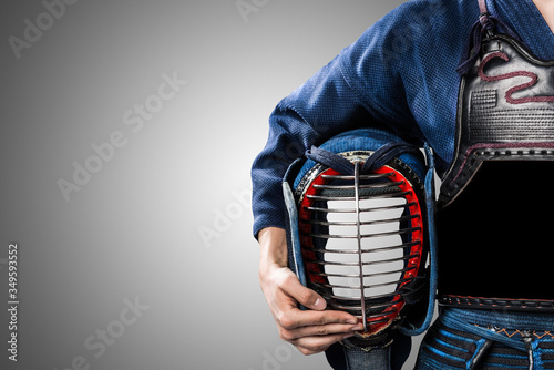 male in in tradition kendo armor with helmet in hand. shot in studio. isolated on grey background