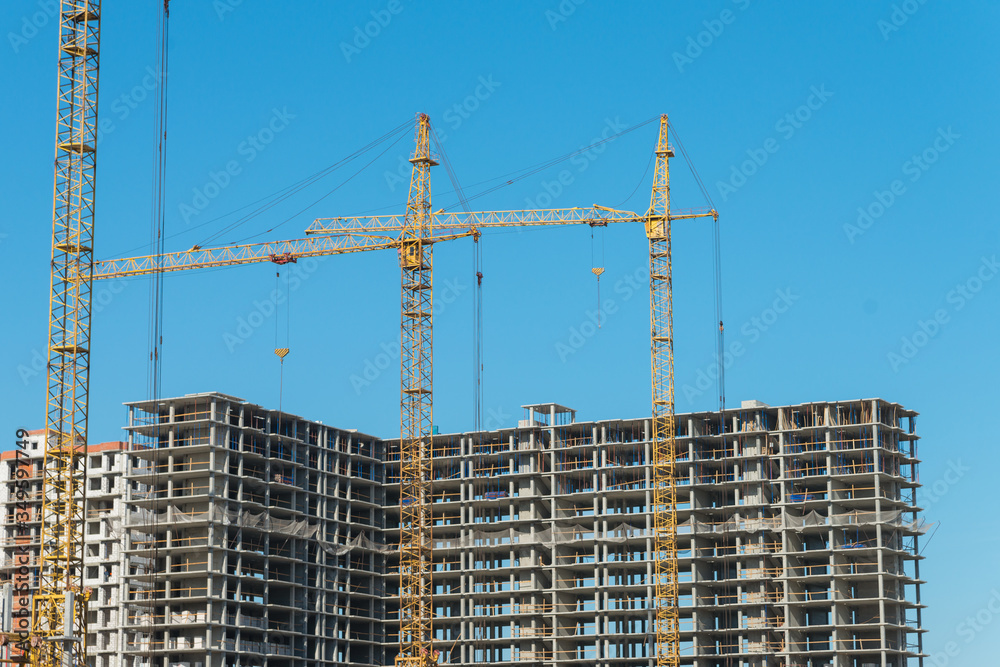 Two construction cranes near the unfinished buildings. Construction and developing Two construction cranes near the unfinished buildings. Construction and developing
