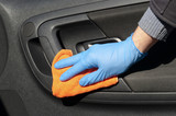 Hand of driver in blue protective glove is wiping with a cloth an interior handle of car door. Coronavirus or Covid-19 car disinfection.