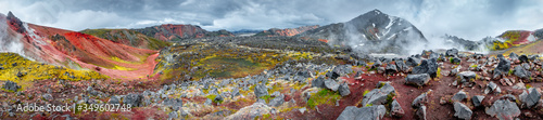 Panoramic landscape view of colorful rainbow volcanic Landmannalaugar mountains and two hikers at hiking trail path with dramatic sky in Iceland, summer, wide angle