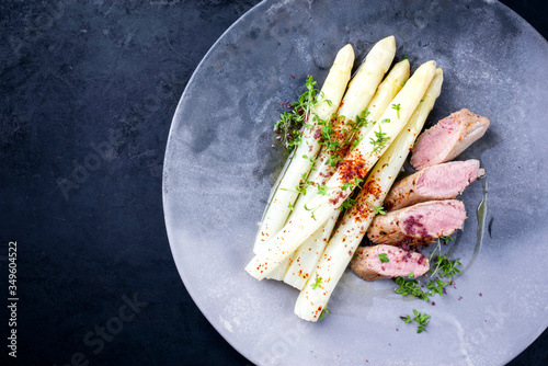 Fried Iberian pork fillet sliced with blanched white asparagus and herbs with spice as closeup on a modern design plate with copy space left