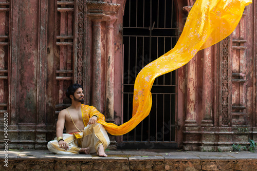 Portrait of an Indian pujari/ worshiper in bare body Indian ethnic traditional wear sitting on a stair of an old abandoned temple. Indian lifestyle and ethnic wear.