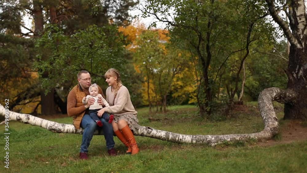 Young parents walking with little daughter in forest in autumn. Beautiful mother talking with girl while father keeping kid while resting in park. Concept of parenthood and autumn. Young parents walking with little daughter in forest in autumn. Beautiful mother talking with girl while father keeping kid while resting in park. Concept of parenthood and autumn.