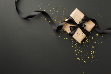 Black Friday sale flat lay with stylish gift box present and ribbon with gold star glitter on black background, flat lay, top view, copy space, xmas and holidays concept