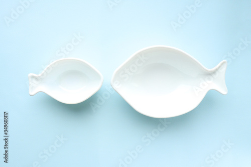 White ceramic empty plates in the shape of fish large and small on a blue background. Selective focus. Table setting.