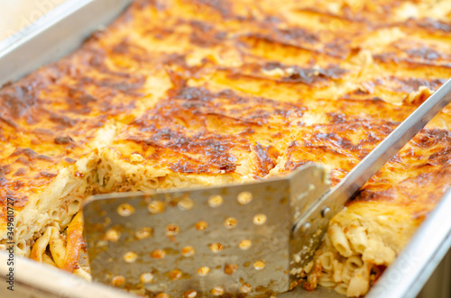 Selective focus on beveled pastitsio dish surface blurry spatula with holes,