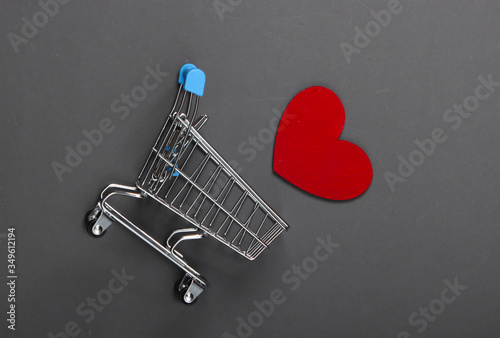 Mini supermarket trolley with red heart on gray background. Shopping lover concept