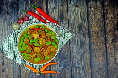 Spicy stir fried shrimps and Parkia nuts with shrimp paste surrounded by key ingredients: garlic, shallot, long fed pepper and yellow chilli on wooden table. photo