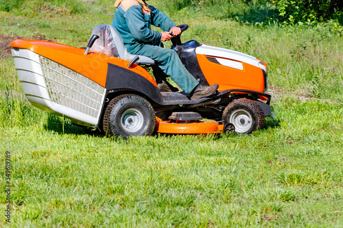 A service worker mows grass with a tractor lawn mower.