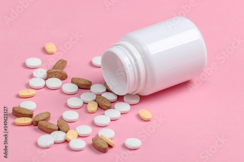 Bottle of different pills on pink pastel background close-up