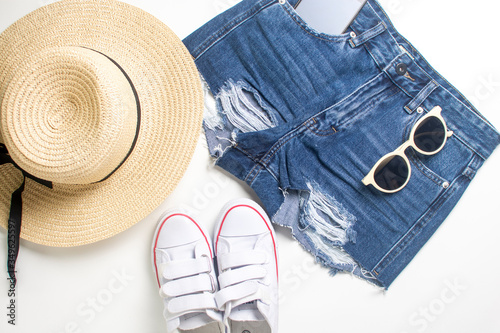 straw, wide brim hat, denim shorts with a phone and sunglasses in pockets and gumshoes isolated on white