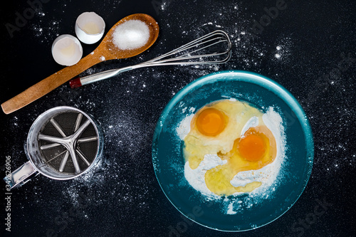 flour and eggs in blue case with beater, sieve, egg shells and sugar in wooden spoon. recipe of cake. cake ingredients. right side