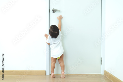 1 year old toddler Asian baby boy standing on tiptoes reaching up try to open door knob,Security and Safety Child Concept.