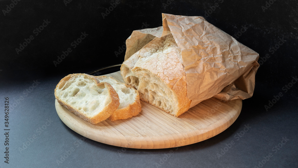 Beautiful bread made from wheat flour on a wooden board on a black background in a paper bag. Sliced slices and half bread.