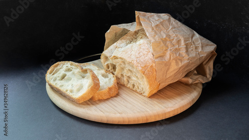 Beautiful bread made from wheat flour on a wooden board on a black background in a paper bag. Sliced slices and half bread.