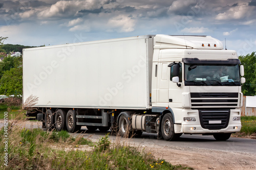 All white long-distance truck with a semitrailer moves in the countryside