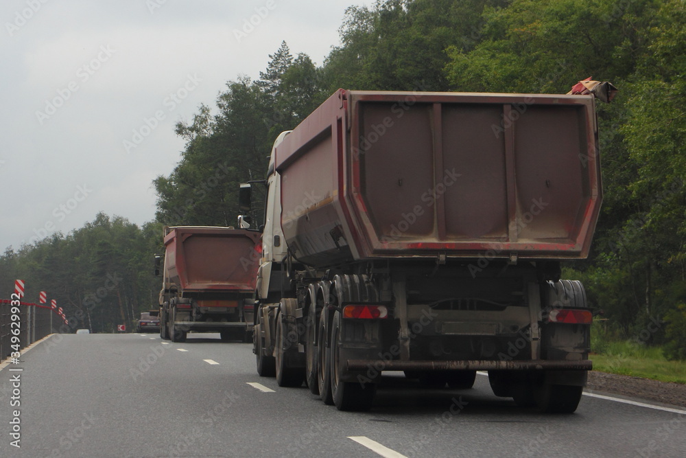 Two heavy dump trucks drive on suburban asphalted highway road at summer day, close up rear-side view – transportation logistics, commercial bulk cargo trucking