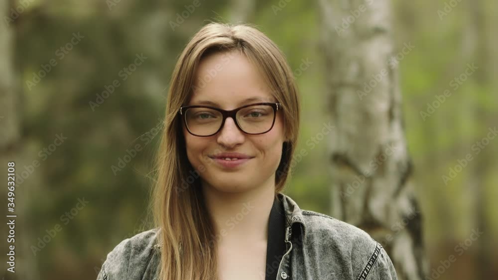 Portrait shot of a young cacasian woman with glasses smiling and noding her head in the park Portrait shot of a young cacasian woman with glasses smiling and noding her head in the park
