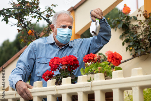 Uomo anziano che indossa un a mascherina chirurgica  con camicia in jeans cura il giardino sotto casa sua photo