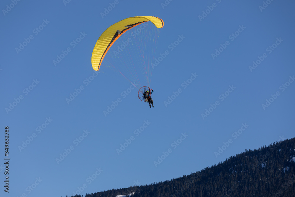 Man flying a paramotor hang glider on a sunny day against a blue sky Man flying a paramotor hang glider on a sunny day against a blue sky