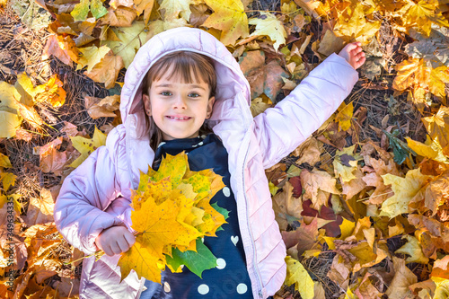 Happy child with maple leaves plays in the park while lying on his back. Golden hour.