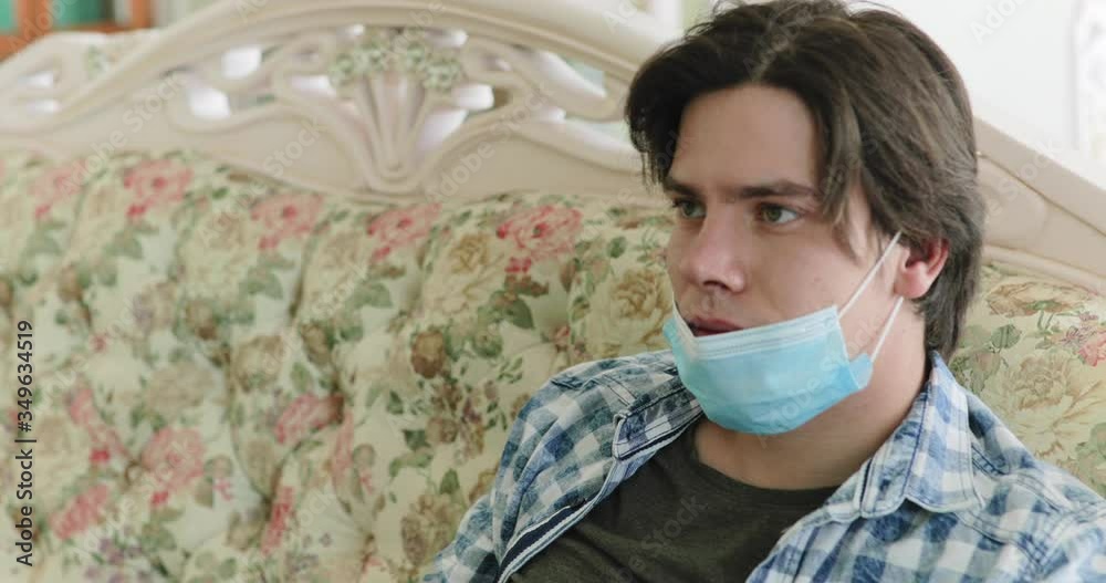 Tired from boring isolation, boy uses tv remote, lowers mask and looks at camera Tired from boring isolation, boy uses tv remote, lowers mask and looks at camera