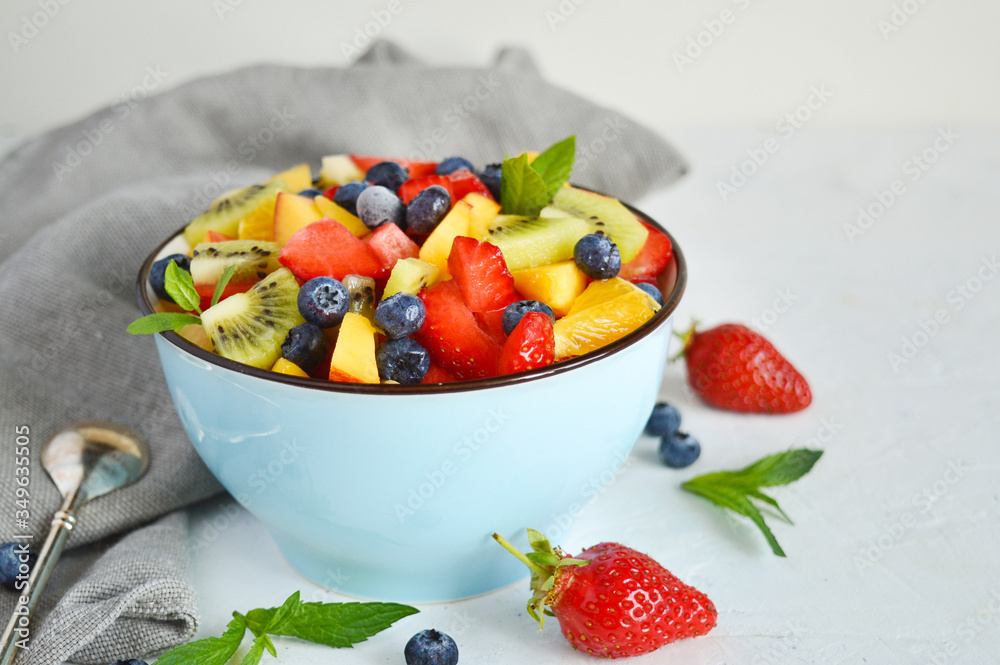 Bowl of vegetarian fresh fruit salad of different fruits: banana, kiwi, apple, orange, strawberry, blueberry on a blue background .The concept of diet, proper nutrition, fitness diet. copy space. Bowl of vegetarian fresh fruit salad of different fruits: banana, kiwi, apple, orange, strawberry, blueberry on a blue background .The concept of diet, proper nutrition, fitness diet. copy space.
