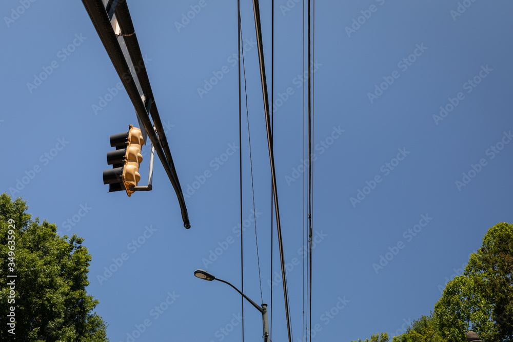 Overhead mast arm with traffic light, power lines and street light against blue sky with trees on lower border, horizontal aspect Overhead mast arm with traffic light, power lines and street light against blue sky with trees on lower border, horizontal aspect