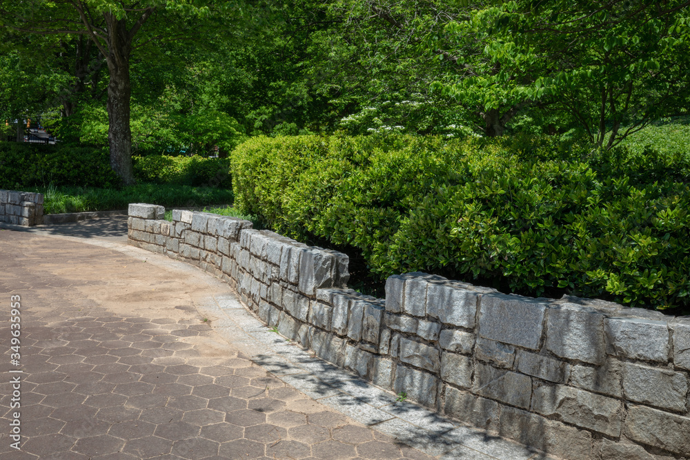 Serpentine rustic granite stone retaining wall in a public park, green trees and bushes, hexagonal paver blocks, horizontal aspect