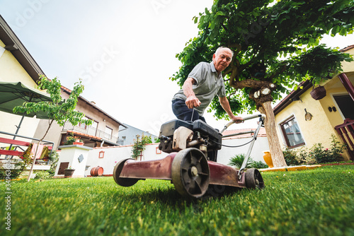 an older man tries to start a lawn mower in the garden, mowing the grass