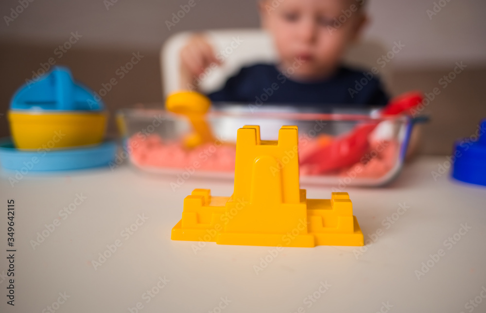 Naklejka premium Yellow plastic fortress in the foreground. Games with sand at home.