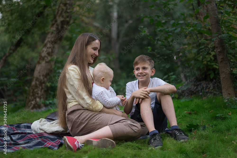 Two children and mom enjoying picnic in summer. Happy family resting in the Park. Two children and mom enjoying picnic in summer. Happy family resting in the Park.