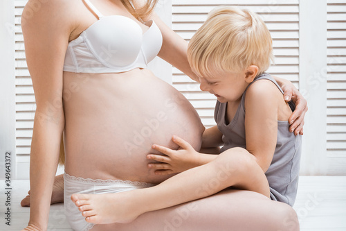 Pregnant woman mother and baby son are hugging. Cute boy touching mom's belly photo