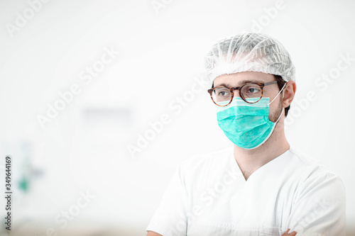 male surgeon with glasses and a surgical hat in a white coat m mask on a white background.
