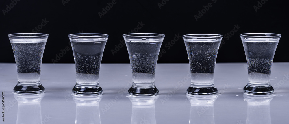 Glasses with vodka on a white table on a black background - obrazy, fototapety, plakaty 