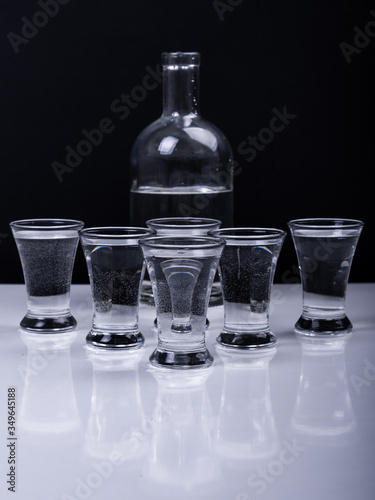 Glasses with vodka and a bottle in the background on a white table and on a black background